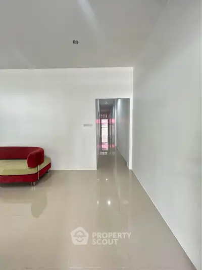 Spacious minimalist living area with modern red sofa and glossy tiled floor.