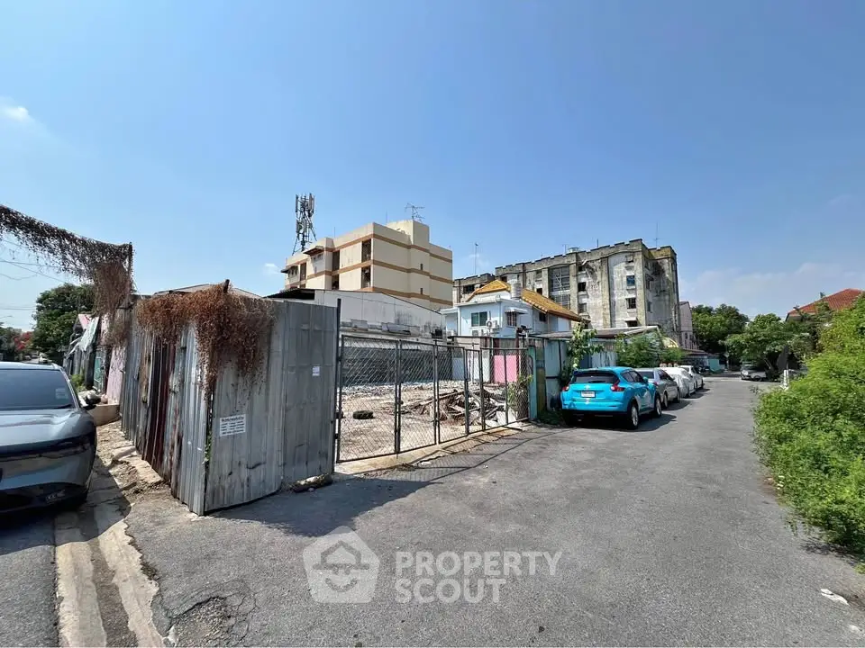 Urban street view with parked cars and residential buildings under clear blue sky.
