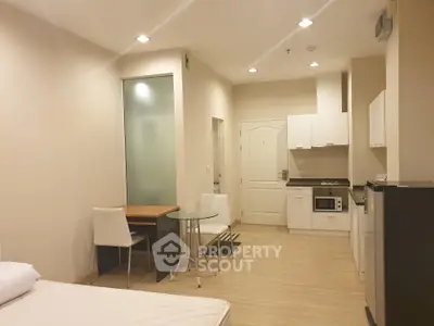 Modern studio apartment with open kitchen and dining area, featuring sleek white cabinetry and cozy lighting.