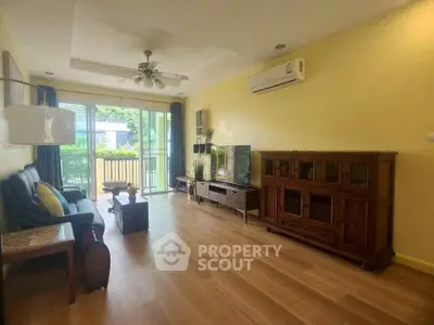 Spacious living room with wooden flooring and large windows opening to a balcony.
