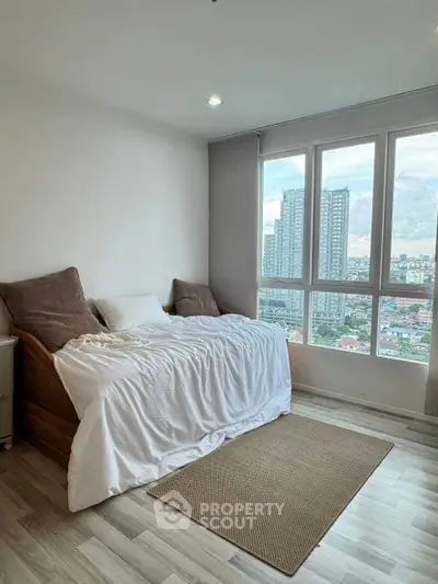 Cozy bedroom with city view, featuring a comfortable bed and large windows for natural light.