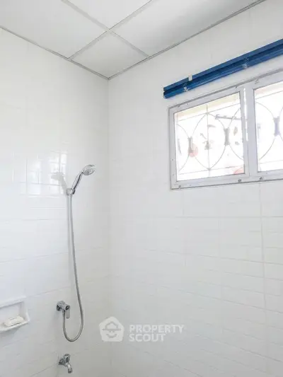 Minimalist bathroom with white tiles and showerhead, featuring a small window for natural light.