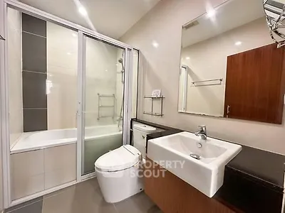 Modern bathroom with sleek fixtures and glass-enclosed bathtub in contemporary apartment.