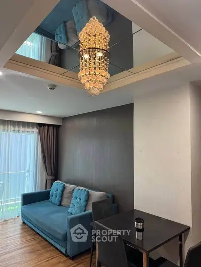 Elegant living room with chandelier and modern decor, featuring a cozy blue sofa and dining area.