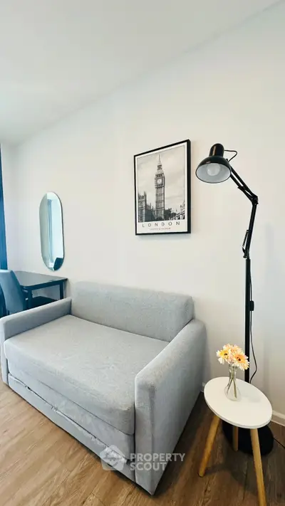 Modern living room with stylish gray sofa, floor lamp, and wall art in a cozy apartment.