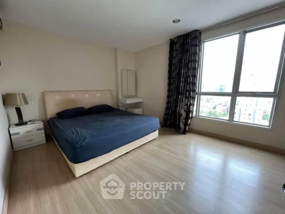 Spacious bedroom with large window and modern furnishings in a high-rise apartment.