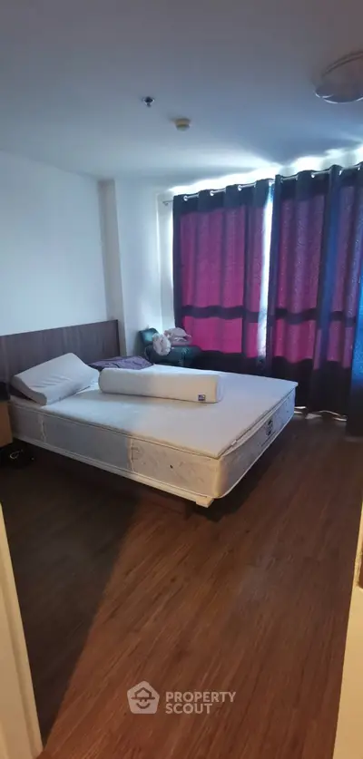 Cozy bedroom with wooden flooring and large window with dark curtains.