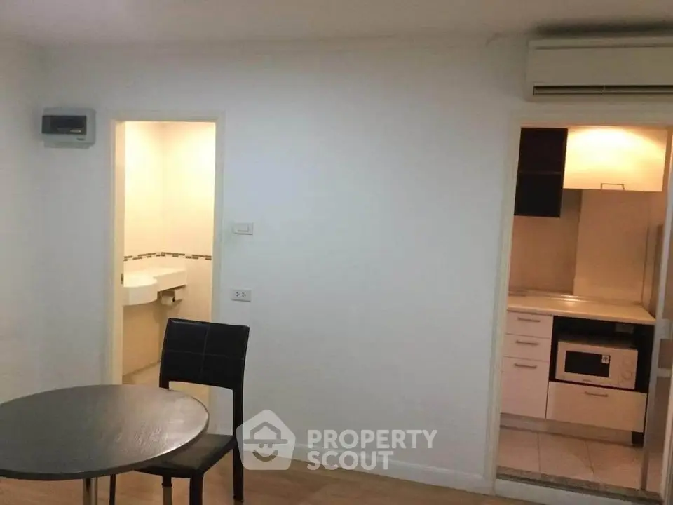 Compact apartment interior with dining area, visible kitchen, and bathroom entrance.