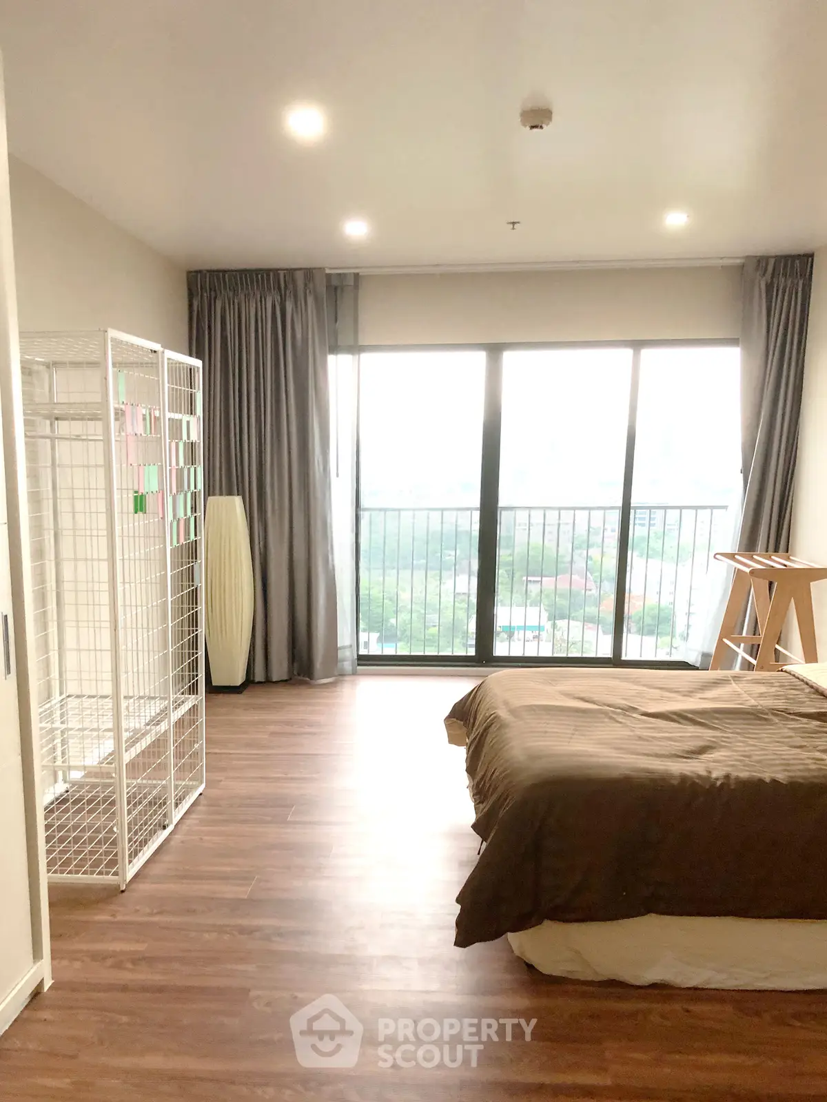 Spacious bedroom with large windows and wooden flooring, offering a serene view.