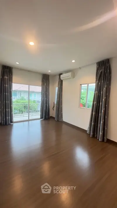 Spacious empty room with large windows and balcony access, featuring elegant curtains and modern lighting.