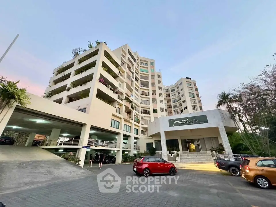 Modern apartment building with lush greenery and spacious parking area at sunset.