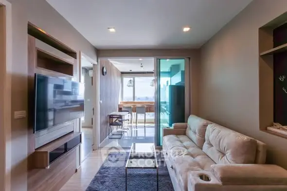 Modern living room with plush sofa and wall-mounted TV, leading to a bright dining area.