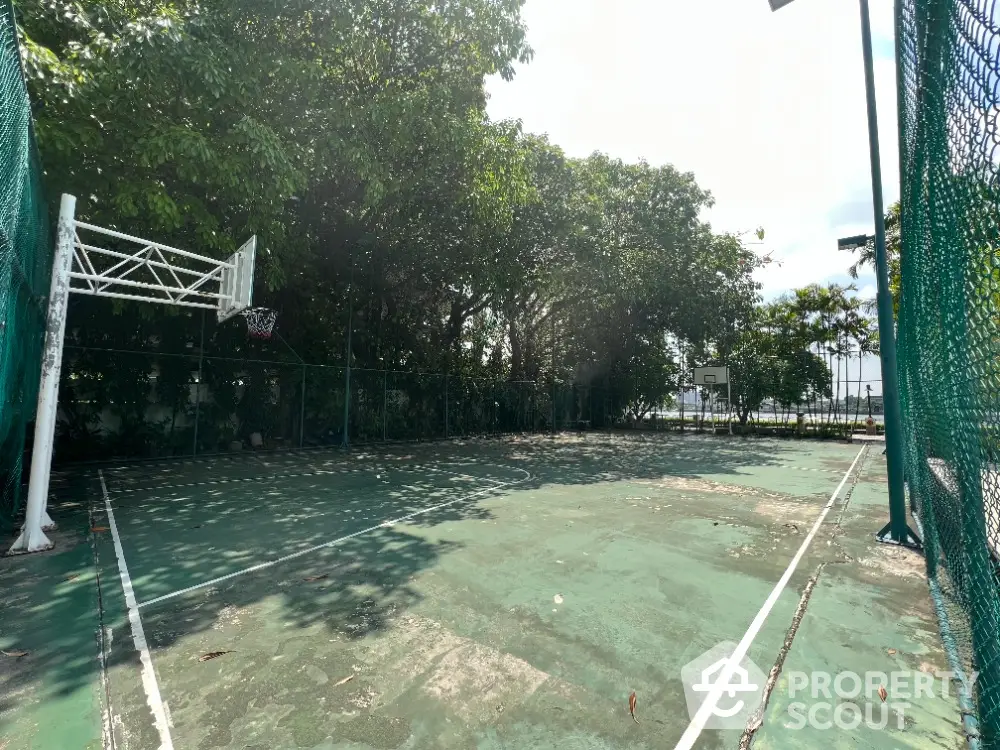 Spacious outdoor basketball court surrounded by lush greenery, perfect for sports enthusiasts in a serene setting.