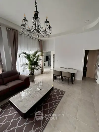 Elegant living room with chandelier, modern furniture, and open kitchen layout.