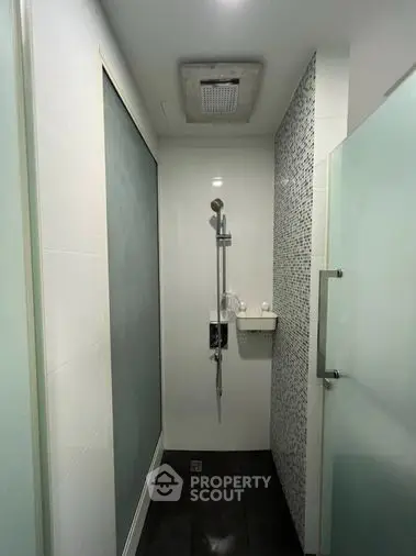 Sleek modern bathroom with a walk-in shower featuring mosaic tiles, a wall-mounted sink, and a frosted glass door for privacy.