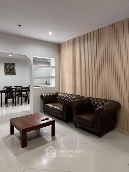 Elegant living room with leather sofas and wooden accent wall, leading to a dining area.