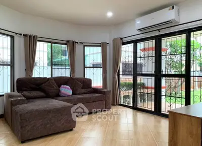 Spacious living room with large windows and garden view, featuring a cozy sectional sofa and air conditioning.