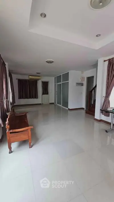 Spacious living room with large windows and elegant curtains, featuring a polished tile floor and modern lighting.
