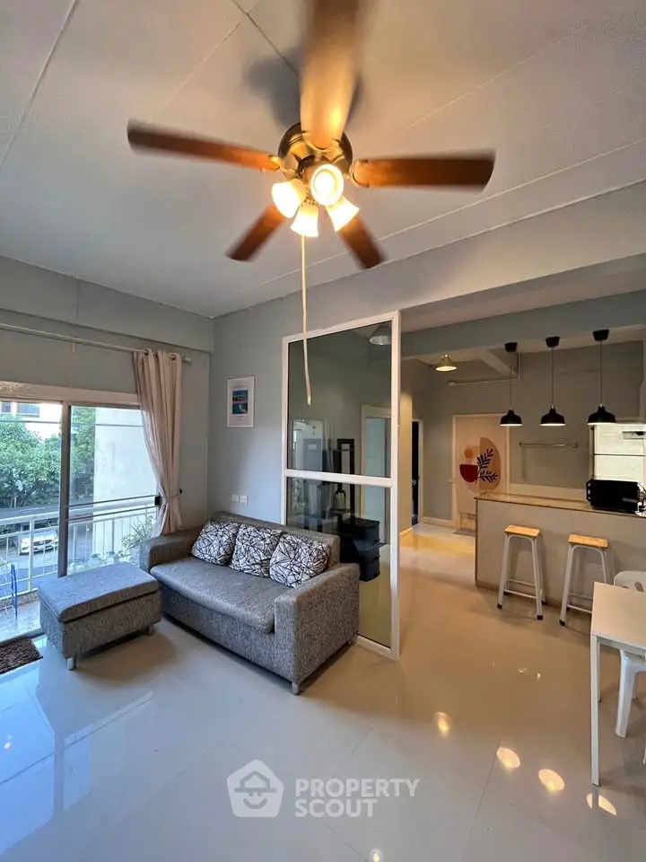 Modern living room with ceiling fan and open kitchen layout, featuring stylish decor and natural light.