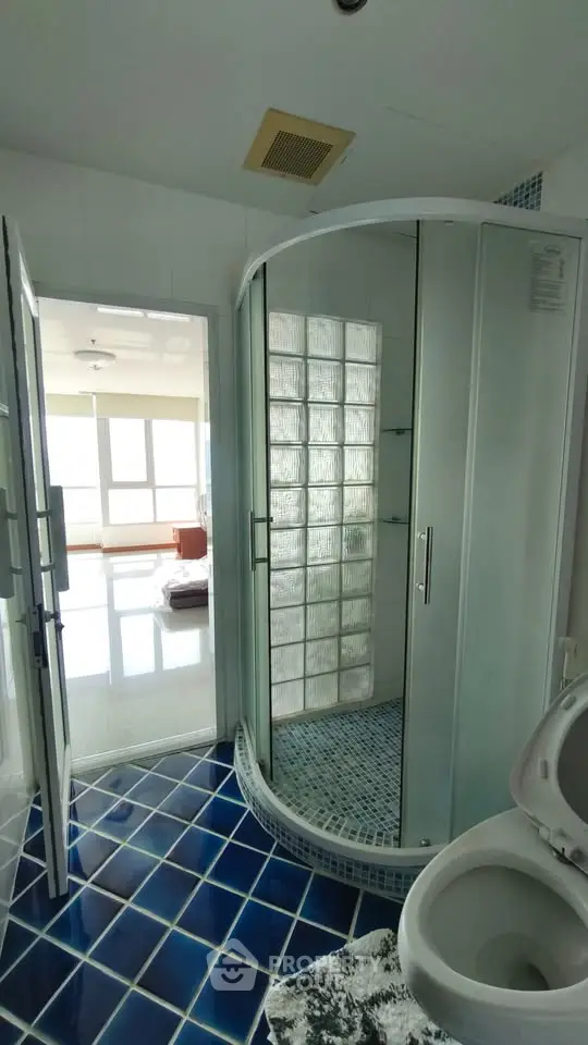 Modern bathroom with glass shower and blue tiled floor in bright apartment