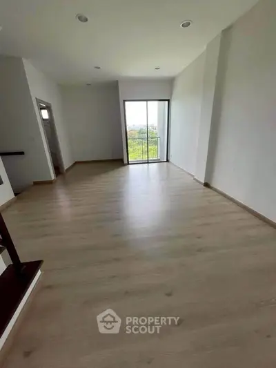 Spacious empty room with wooden flooring and balcony view