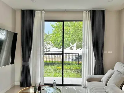 Modern living room with large window and elegant curtains overlooking a lush garden.