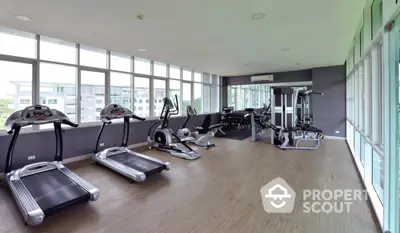 Spacious modern gym with large windows and state-of-the-art equipment in luxury building.