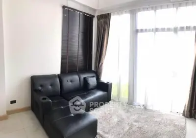 Modern living room with sleek black sofa and large windows for natural light.