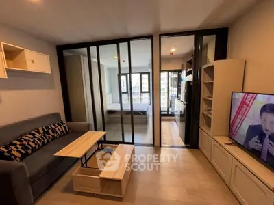 Modern living room with sliding glass doors leading to a bedroom, featuring stylish furniture and a TV.