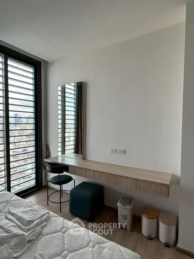 Modern bedroom with city view, featuring a sleek desk and comfortable seating.