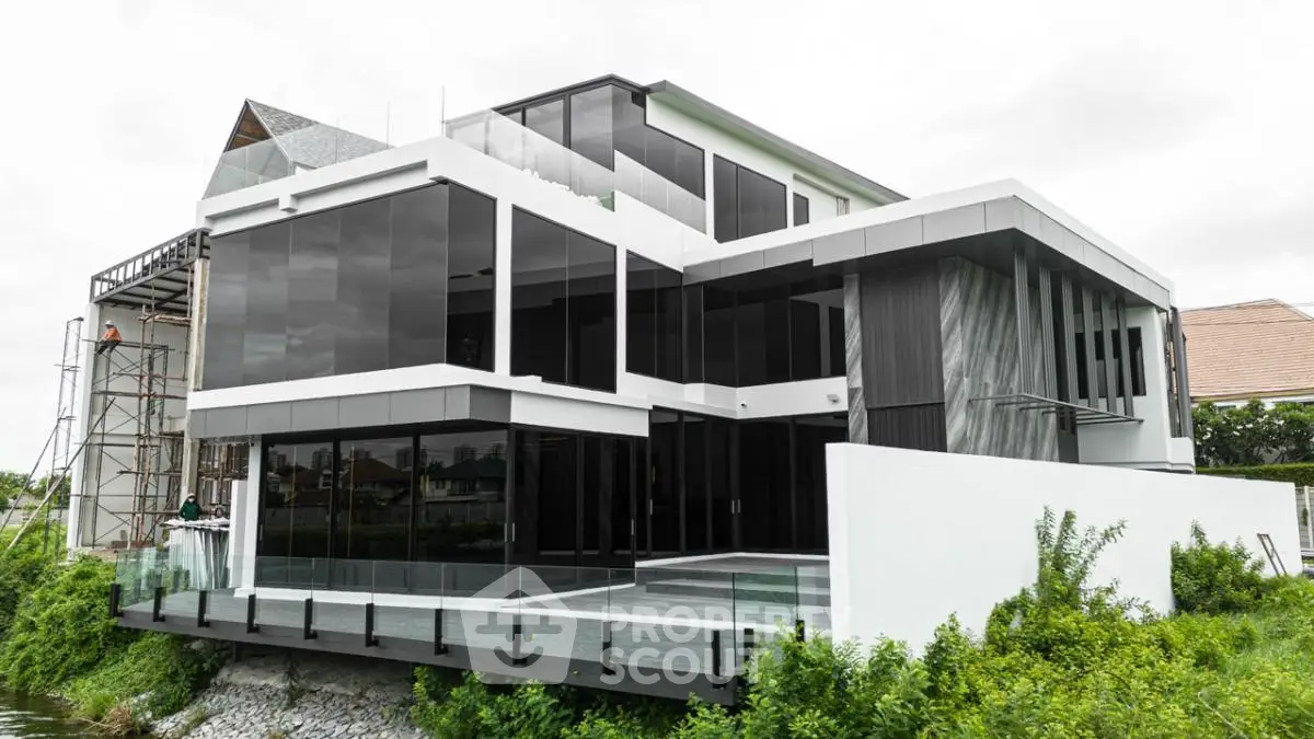 Modern luxury home with sleek glass facade and spacious balcony overlooking lush greenery.