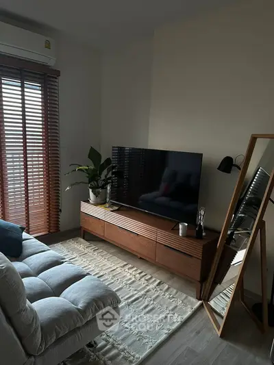 Cozy living room with modern decor, large TV, and natural light from wooden blinds.