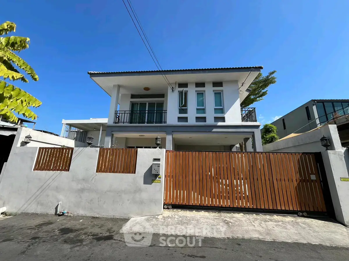 Modern two-story house with wooden gate and balcony under clear blue sky