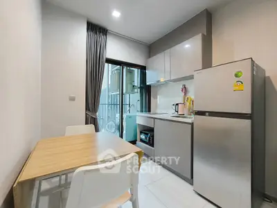 Modern kitchen with sleek cabinets, dining table, and stainless steel fridge in a cozy apartment.