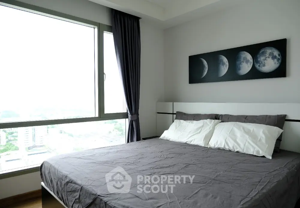 Modern bedroom with large window and moon phase artwork, offering a serene city view.