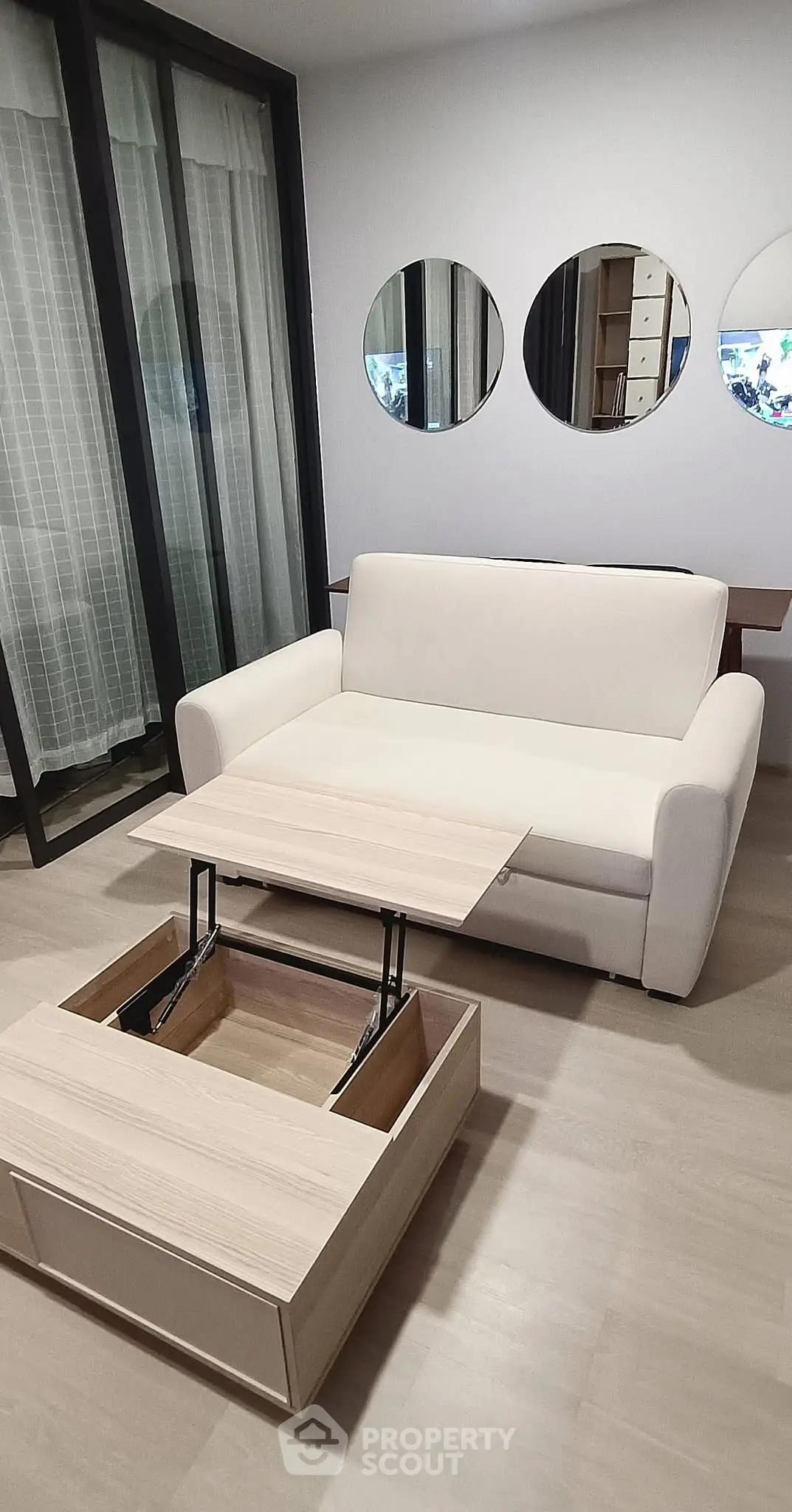 Modern living room with convertible coffee table and white sofa, featuring stylish round mirrors.