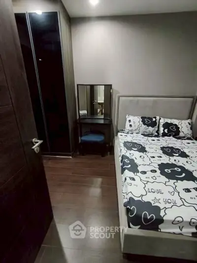 Cozy bedroom with stylish decor and wooden flooring, featuring a comfortable bed and a small vanity area.