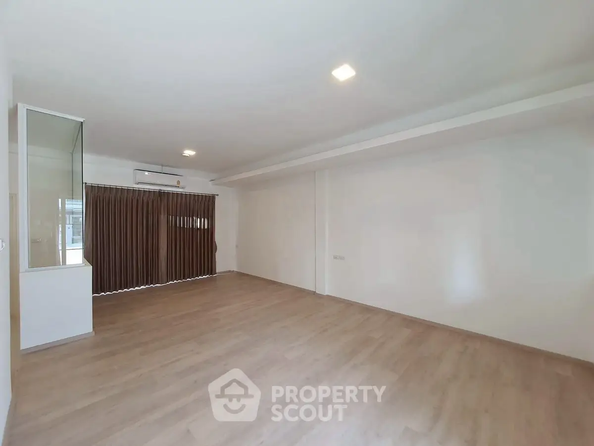 Spacious empty living room with wooden flooring and large window, perfect for customization.