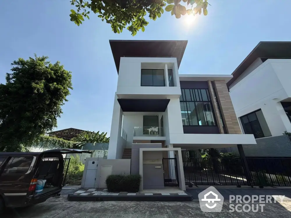 Modern three-story house with sleek design and large windows in a sunny neighborhood.