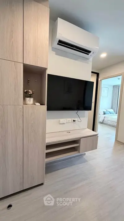 Modern living room with sleek TV setup and air conditioning, leading to a cozy bedroom.