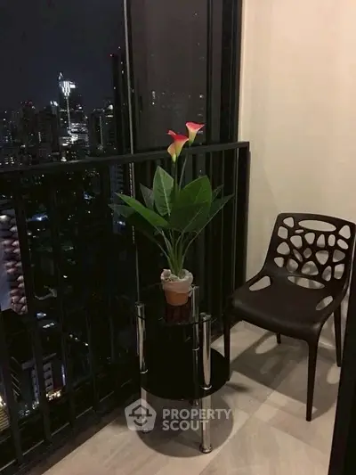Chic city balcony with modern chair and plant, offering stunning nighttime skyline views.