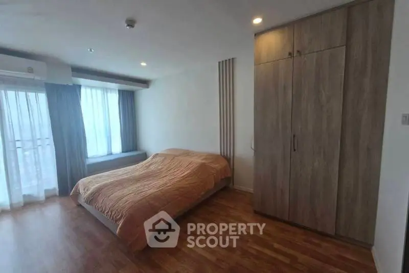 Spacious bedroom with wooden flooring and large window for natural light.