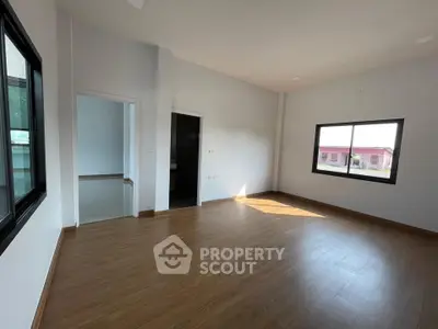 Spacious empty room with wooden flooring and large windows offering natural light.