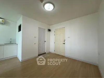 Spacious minimalist apartment interior with wooden flooring and white walls, featuring a compact kitchen area.