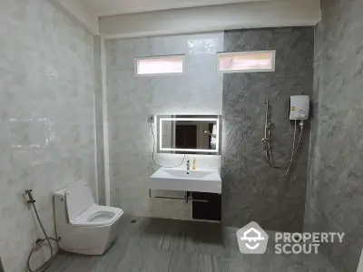 Sleek modern bathroom with wall-mounted sink, large mirror, and stylish tiling, featuring a water heater and a high-tech toilet, perfect for contemporary living.