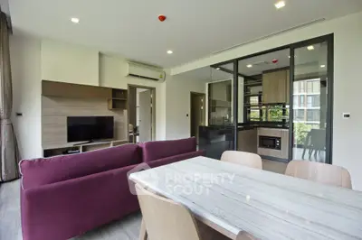Modern open-plan living room with stylish kitchen and dining area, featuring sleek furniture and natural light.