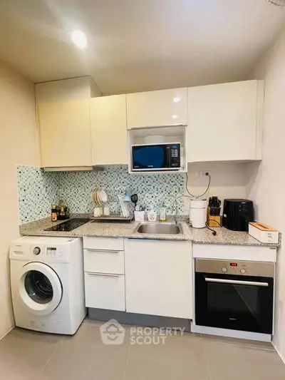 Modern kitchen with washing machine, oven, and microwave in compact layout.