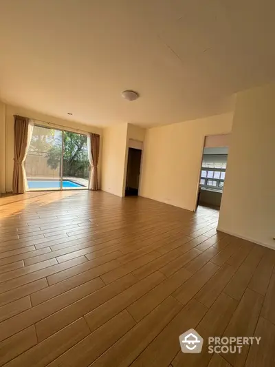 Spacious living room with wooden flooring and pool view, perfect for relaxation.