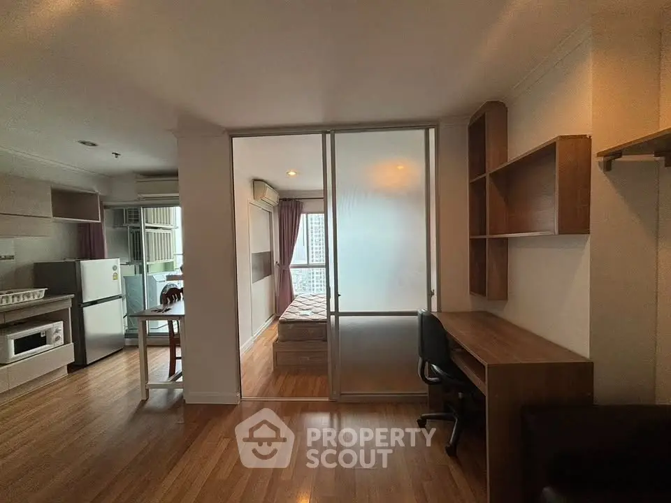 Modern apartment interior with open kitchen and study area, featuring wooden flooring and glass partition.