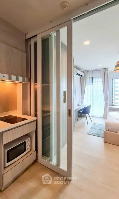 Modern studio apartment with open kitchen and cozy bedroom area, featuring sleek sliding glass doors.